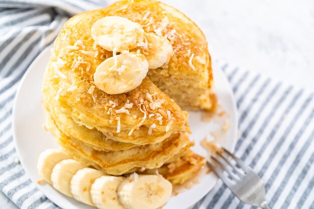 Photo eating freshly baked coconut banana pancakes garnished with sliced bananas and toasted coconut