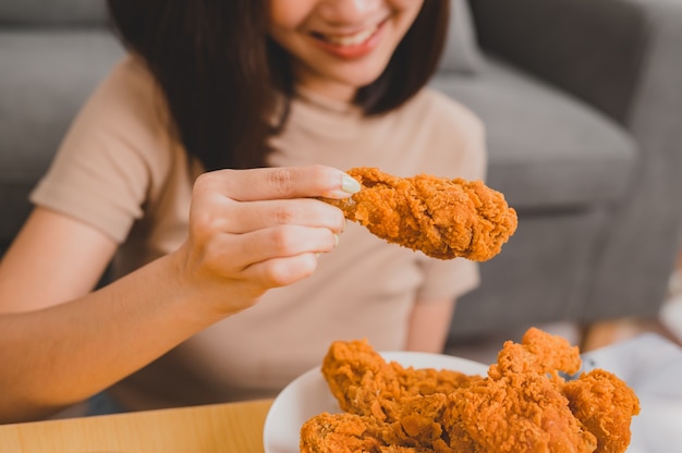 Mangiare pollo fritto durante l'asporto e la consegna. fast food da asporto a casa. stile di vita della donna asiatica in soggiorno. distanziamento sociale e nuova normalità.