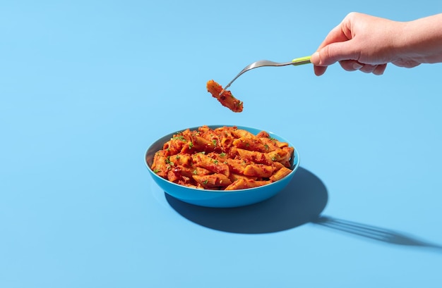 Eating pasta penne alla arrabbiata from a bowl minimalist on a blue background