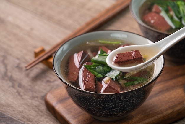 Eating pig blood soup, homemade Taiwanese traditional food with pickled mustard greens and garlic sprouts in a bowl on wooden table.