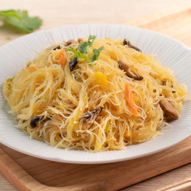 Mangiare spaghetti di vermicelli di riso saltati in padella con zucca bollita e verdure su sfondo tavolo in legno
