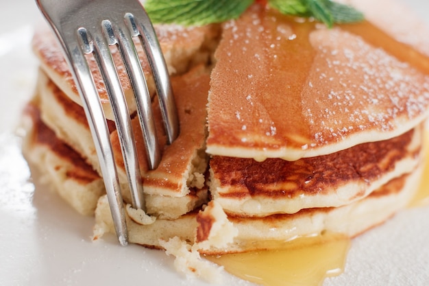 Eating sweet american pancakes with honey closeup. Crepe and fork on white plate background. Traditional US meal.