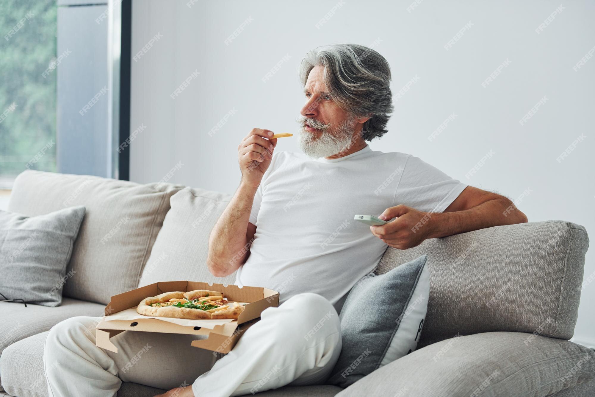 Premium Photo | Eats delicious pizza while watching tv show senior stylish  modern man with grey hair and beard indoors