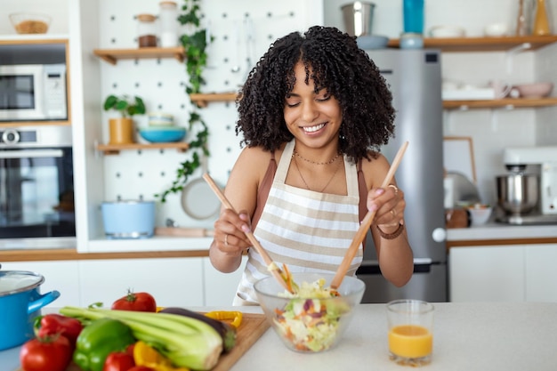 Eautiful cute young smiling woman on the kitchen is preparing a vegan salad in casual clothes