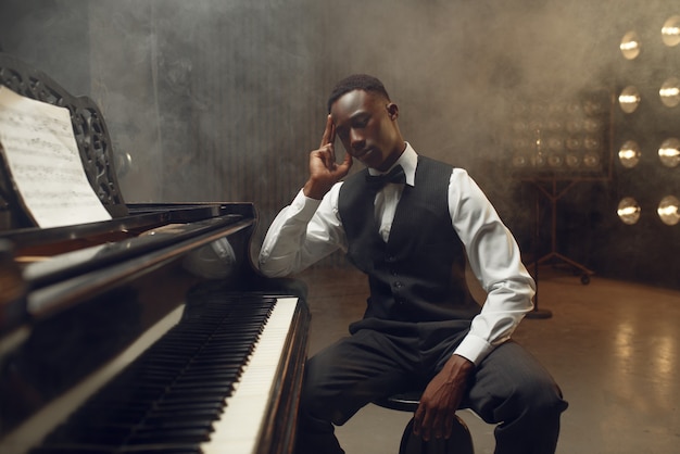 Ebony grand piano player, jazz performer on the stage with spotlights. musician poses at musical instrument before concert