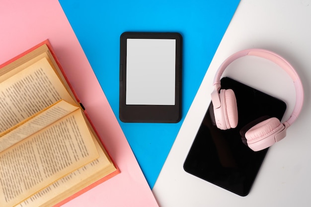 Ebook reader digitale tablet met koptelefoon en boek op kleurpapier achtergrondstudiofoto