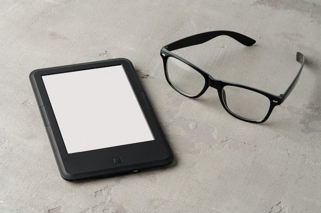 Ebook reader with glasses on gray background close up