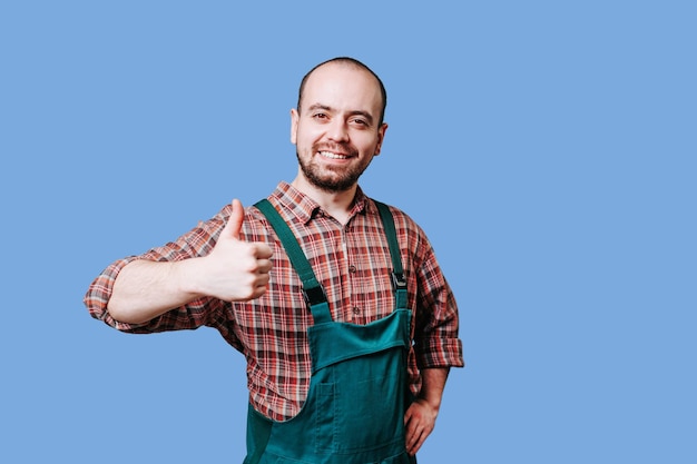 An ebullient young farmer with a beard is photographed in overalls giving a thumb up and standing in