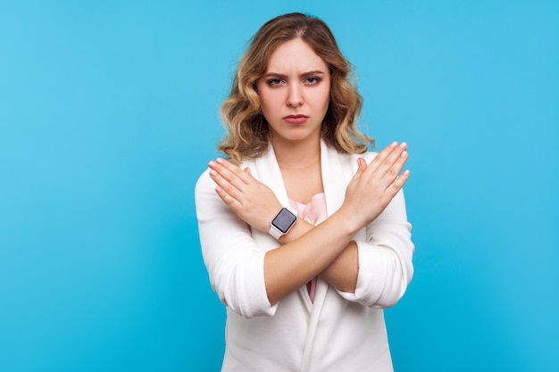 Echt niet, nooit meer. Portret van een vastberaden serieuze vrouw met golvend haar in een witte jas die de handen op de borst kruist, x-teken gebarend, stop, dit is klaar. indoor studio-opname geïsoleerd op blauwe achtergrond