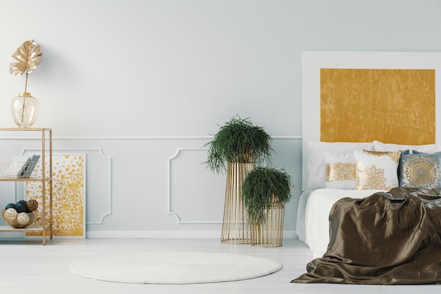 Echte foto van een glamour slaapkamer interieur met planten in gouden potten bed en muur lijstwerk