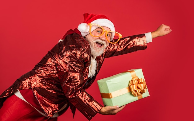 Echte gevoelens grappige senior man in kerstman kostuum gelukkig nieuw 2021 jaar vrolijk kerstfeest bebaarde kerstman in hoed vliegen op rode achtergrond kerstcadeautjes en cadeau winkeltijd wintervakantie vreugde