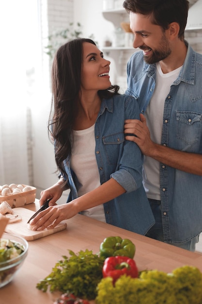 Echtgenoot omhelst vrouw die champignons op het houten bord snijdt en naar elkaar kijkt