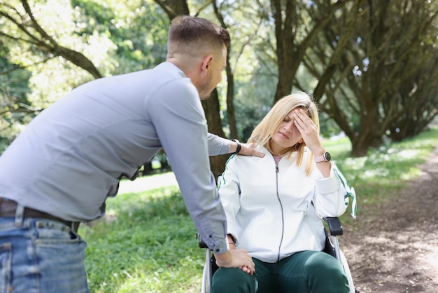 Echtgenoot troost vermoeide vrouw op een rolstoel in het park close-up hoofdpijn stress revalidatie