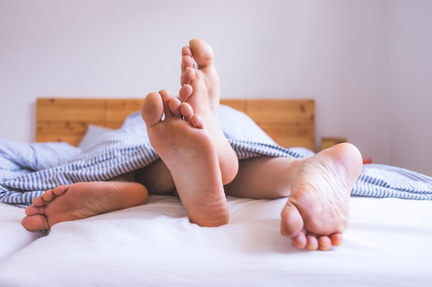 Echtpaar geniet van de ochtend in bed Close-up van onbedekte voeten in de beddeken