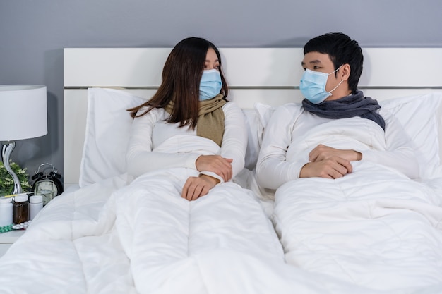 Echtpaar in medische maskers praten samen op bed, bescherming tegen pandemie concept coronavirus.