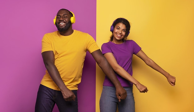 Echtpaar met hoofdtelefoon luisteren naar muziek en dansen met energie op violette en gele achtergrond