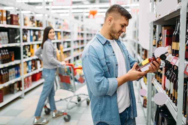 Echtpaar met kar in supermarkt, afdeling alcoholische dranken, familie winkelen. Klanten kiezen dranken in de winkel, kopers op de markt