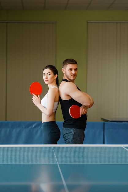 Echtpaar met rackets vormt op de tafeltennistafel met net binnenshuis.