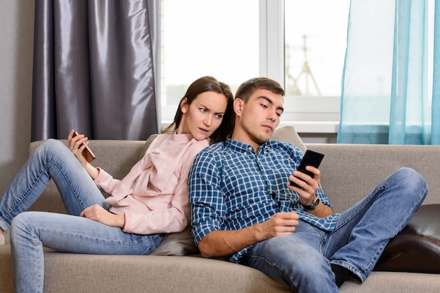 echtpaar zittend op de bank en met behulp van smartphones, vermoedt de vrouw dat de man zijn telefoon bespioneert