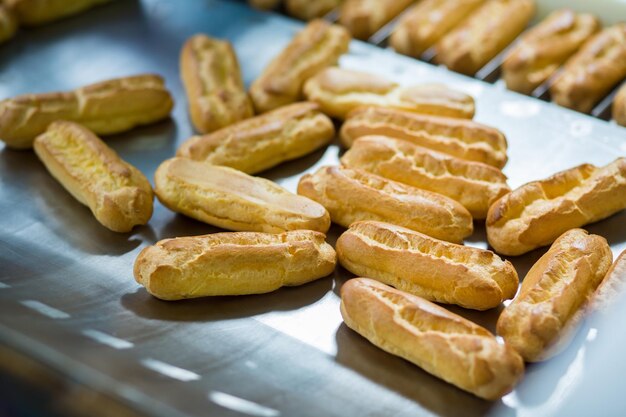 Eclair-schelpen op metalen oppervlak Gele deegproducten Ingrediënt voor smakelijk dessert Vers gebakken goederen in de fabriek