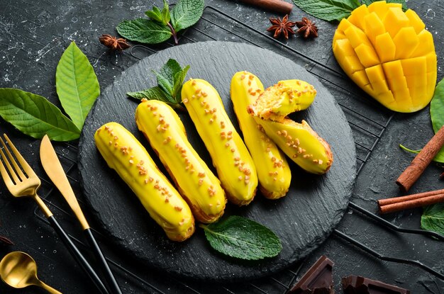 Eclair with mango cream Mango dessert on a black stone plate Top view Rustic style