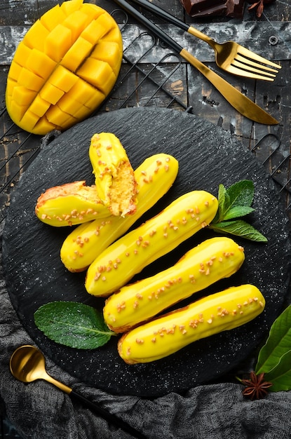 Eclair with mango cream Mango dessert on a black stone plate Top view Rustic style