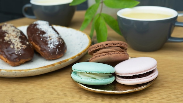 Eclairs en macarons op een tafel met theekopjes in een café Zoet voedsel Stilleven