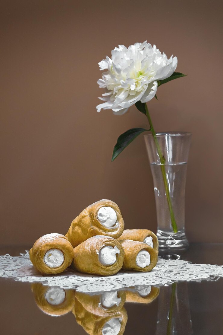 Photo eclairs lie on a napkin behind a vase with a white flower