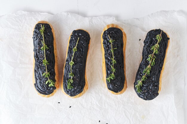 Eclairs met pistacheroom en zwarte glazuur. Taarten versierd met takjes tijm. Dessert op de witte keukentafel.