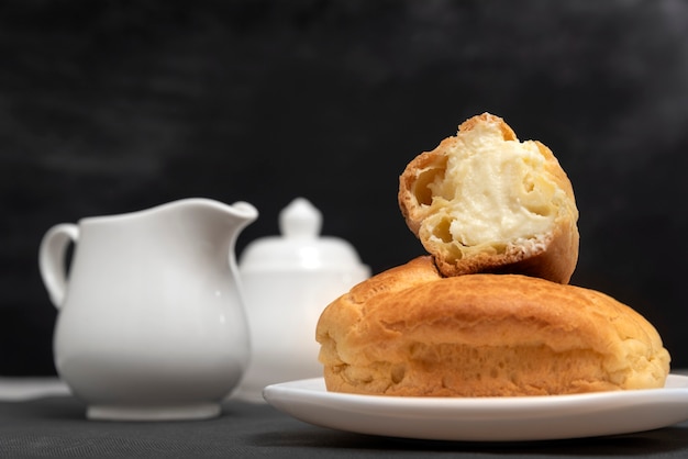 Eclairs met roomvulling op plaat naast kruik. zoet gebak, close-up. bakken voor thee. zelfgemaakte soesjes.