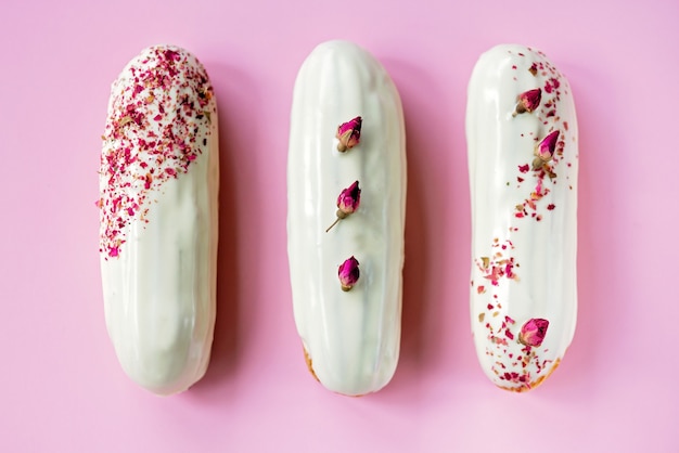 Eclairs of soesjes met roze smaak witte chocolade glazuur op roze achtergrond.