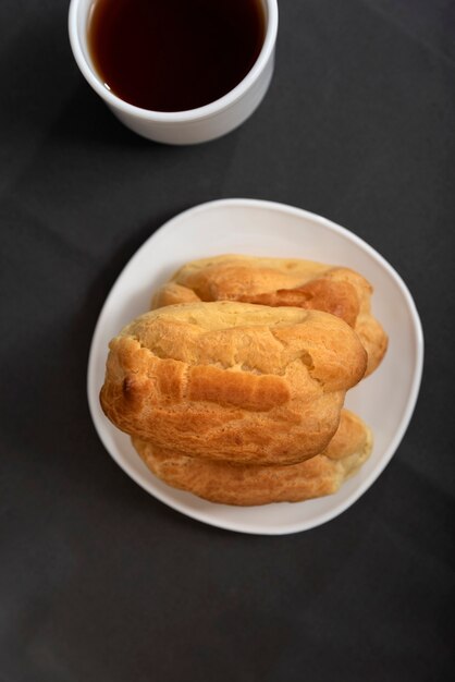 Eclairs on plate and cup of tea top view. Profiteroles on saucer on gray background. Baking for tea.