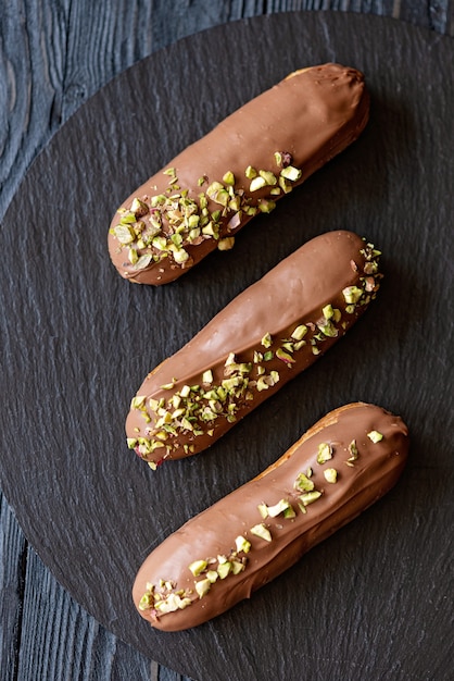 Eclairs o profiteroles con latte, glassa al cioccolato e pistacchi su una piastra nera vista dall'alto