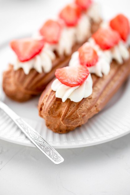 Photo eclairs with cream and strawberries and a cup of tea on a white plate