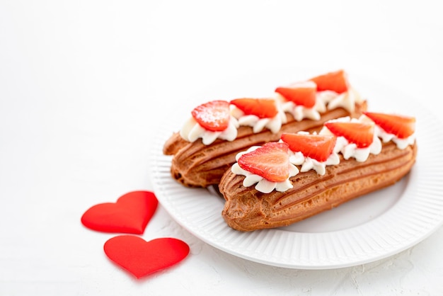 Eclairs with cream and strawberries on a white plate valentines day concept