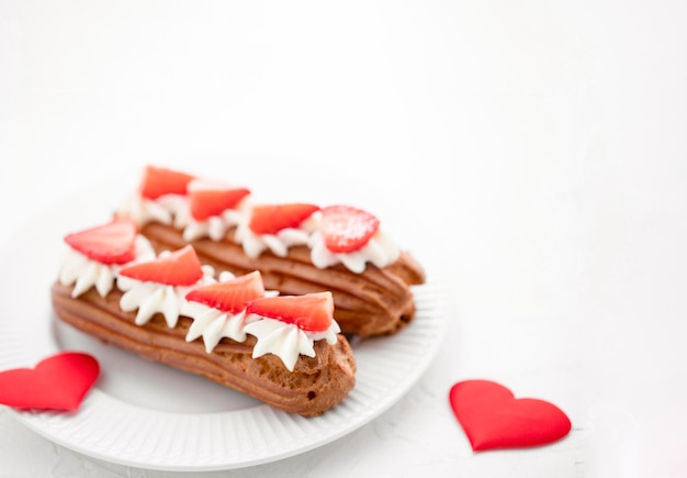 Eclairs with cream and strawberries on a white plate Valentines Day Concept