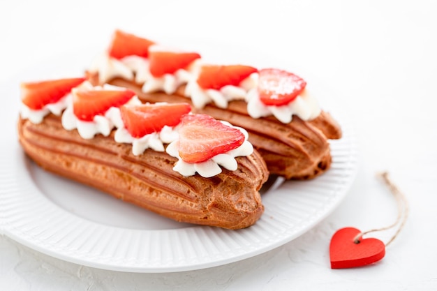 Eclairs with cream and strawberries on a white plate valentines day concept