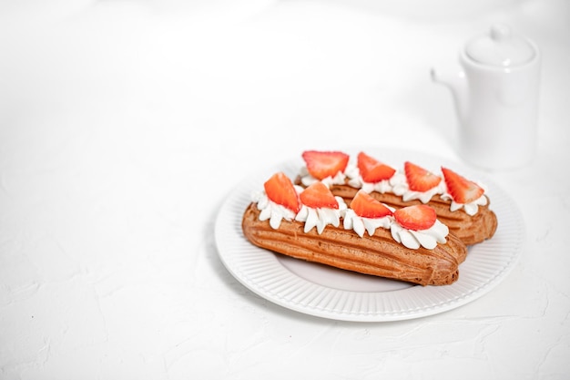 Eclairs with cream and strawberries on a white plate