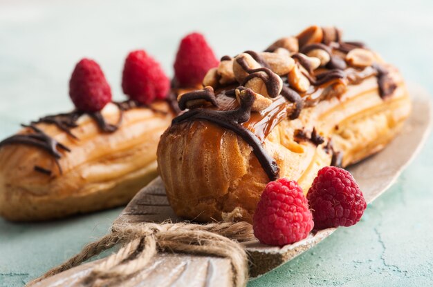 Eclairs with peanuts, chocolate icing and raspberries