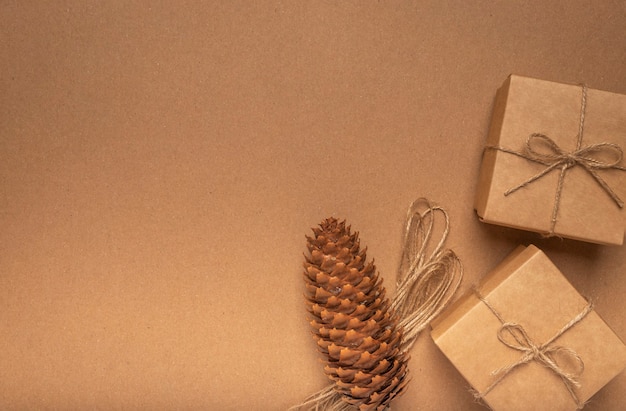 Eco background of craft cardboard texture with two gift boxes, pine cone and jute string.