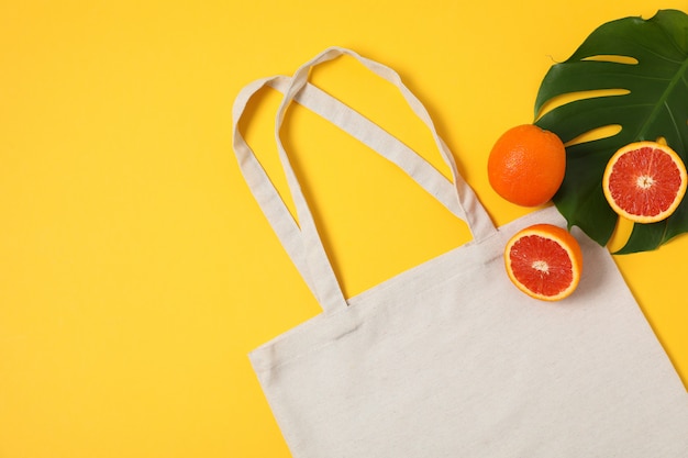 Eco bag, palm leaf and orange on color background