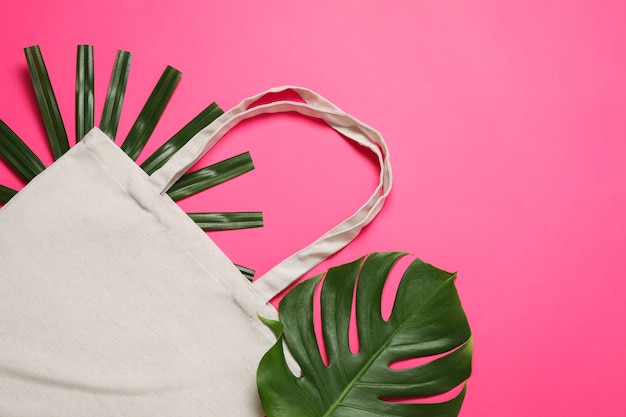 Eco bag and palm leaves on color background