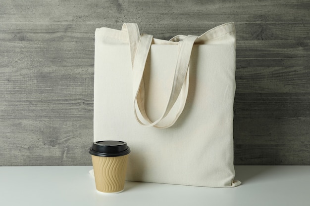 Eco bag and paper cup against gray textured surface