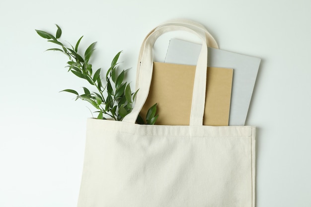 Photo eco bag with copybooks and twig on white surface