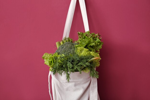 Eco bag with fresh vegetables hanging on wall