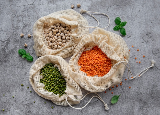 Eco bags with different types of legumes on a brown surface