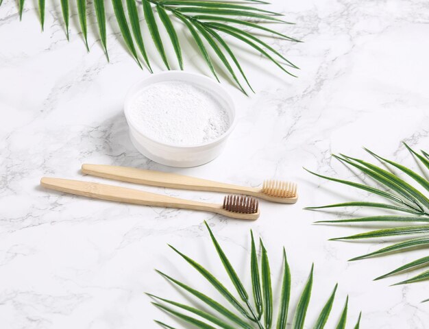 Eco bamboo toothbrushes and dentifrice with palm leaves on a marble background Dental care concept