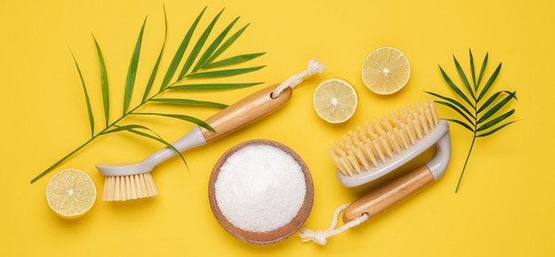 Eco brushes, sponges, lemon, leaves and soda on yellow background