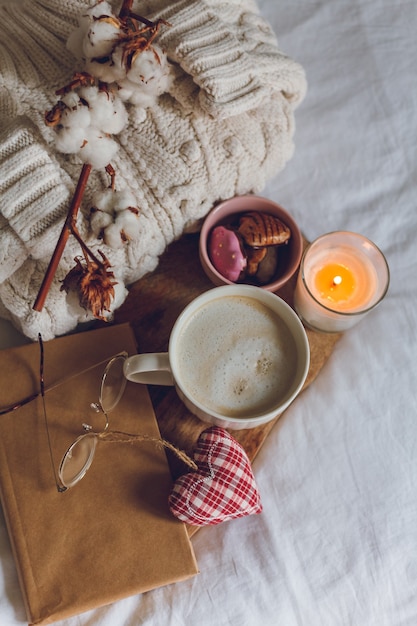 Eco decor for the home. Home cozy decor. A mug of cappuccino, cookies, a candle on the bed. Winter morning. Holidays.