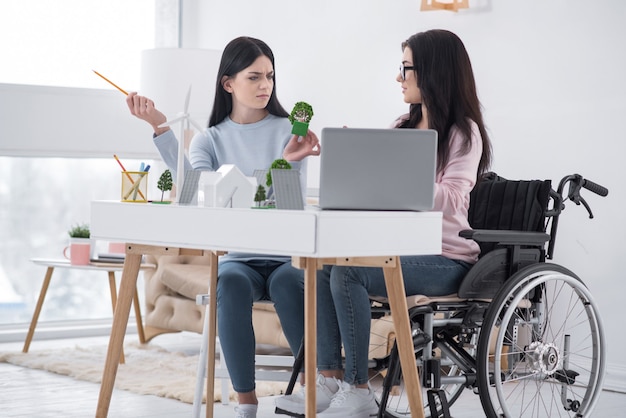 Eco dorp. lage hoek van ongemakkelijke onbeweeglijke vrouw en collega poseren aan tafel tijdens ruzie